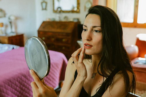 Fashionable woman putting makeup in her apartment in Italy.