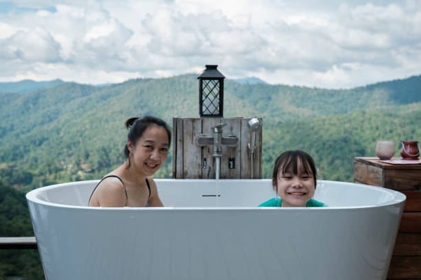 Mum and child relax in bathtub in panoramic mountain range view.