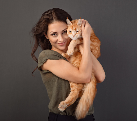 Beautiful make-up woman with toothy smile holding and tender hugging with love her red maine coon kitten. Closeup  portrait on toned color background with empty copy space