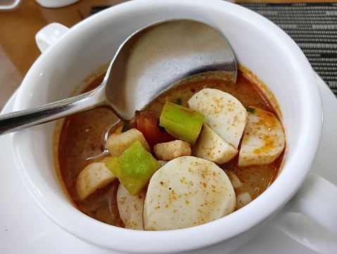 tomyam in white ceramic bowl, spoon. close up.