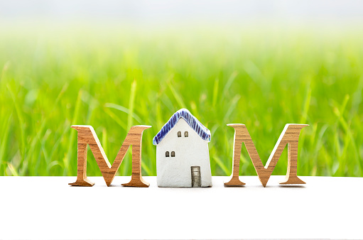 M wooden font with miniature vintage house model over blurred green grass background, mother's day card background idea