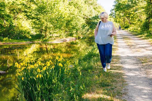 Mature woman with smartphone, strolling on the natural trail along the historical Walnutport Canal in Pennsylvania