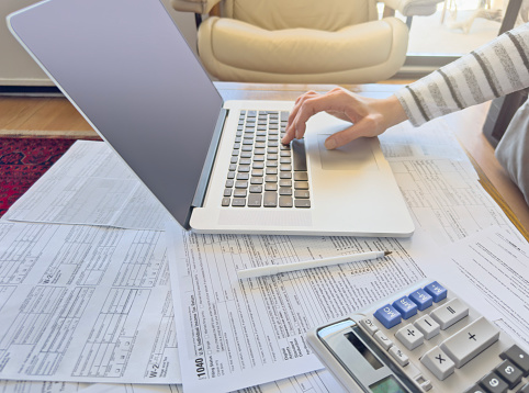 Close up photo of a woman doing taxes with laptop and tax forms in a house