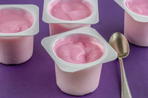 Pink yogurt cup with defocused cups on purple background - kid yogurt - condensation on the cold cups