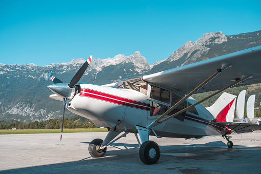 A single-engine light aircraft parked on a tarmac against a backdrop of towering mountains, prepared for a scenic flight experience.