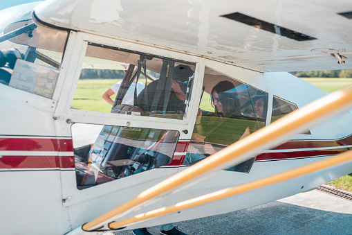 A diverse group of tourists seen through the windows of a small airplane, preparing for a panoramic flight on a sunny day. Safety procedures are performed before takeoff.