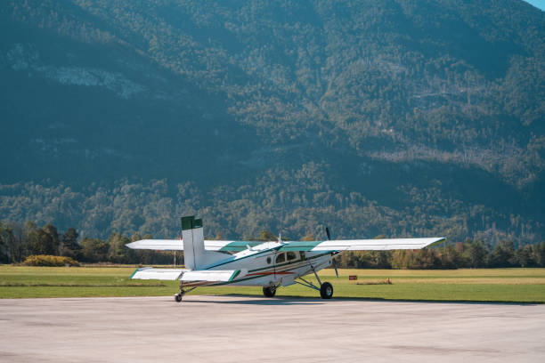 A single-engine light aircraft parked on a tarmac against a backdrop of towering mountains, prepared for a scenic flight experience.