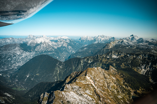 A panoramic view of rugged mountain peaks seen from the vantage point of an airplane window, showcasing the natural beauty and topography of the region from a high-altitude perspective.