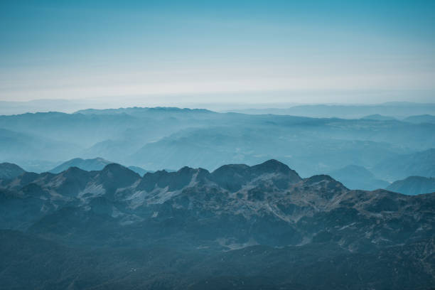 An expansive aerial shot captures the serene beauty of layered blue mountains, observed from a panoramic flight, ideal for travel and nature themes.