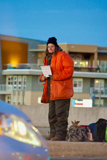 Denver, Colorado, USA - February 12, 2024: An unidentified woman holds a handmade sign with the words “Anything Helps, God Bless” at a busy intersection in the Mile High City on a cold winter evening.