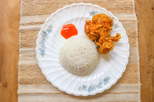 Crispy fried chicken with spicy sauce is served with rice and vegetables such as cucumber, tomato and celery as garnish. Fried chicken and rice on wooden table