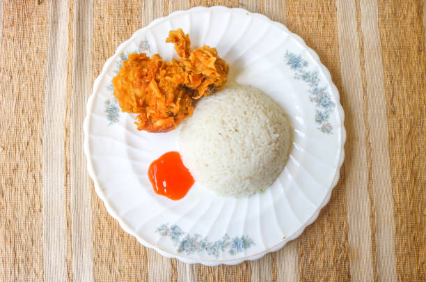 Crispy fried chicken with spicy sauce is served with rice and vegetables such as cucumber, tomato and celery as garnish. Fried chicken and rice on wooden table