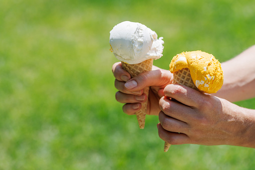 Woman's hands holding refreshing ice cream in waffle cones treats with a hint of zesty lemon flavour. With copy space