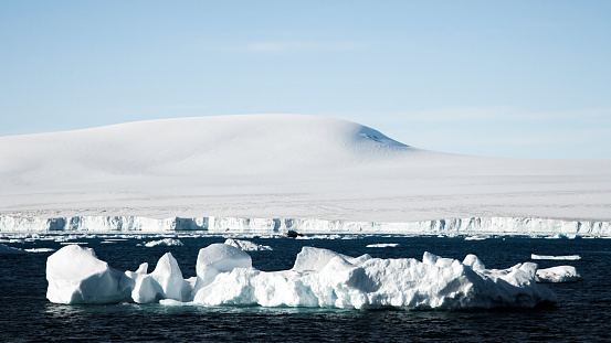 Icebergs drifting in front of snow-capped Antarctica Coast under light sunny skyscape. Antarctica Peninsula Coast, Antarctica