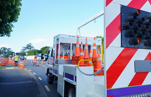 Work truck loaded with Road Closed signs and orange traffic cones. Unrecognizable workers put traffic cones on the road. Roadworks in Auckland.