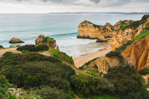 Captivating scene of a rugged shoreline with natural arches and caves, crashing ocean waves, a dramatic beachscape, and a cloudy sky. Algarve, Portugal