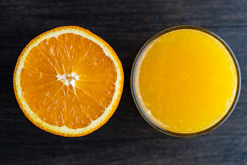 Half an orange and a glass of freshly squeezed orange juice on a wooden background, close up, top view