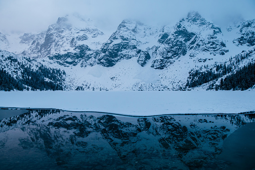 An atmospheric natural landscape with a Morskie Oko lake reflecting snowcovered mountains, creating a serene and picturesque scene with a snowy slope and ice caps. Tatry, Poland