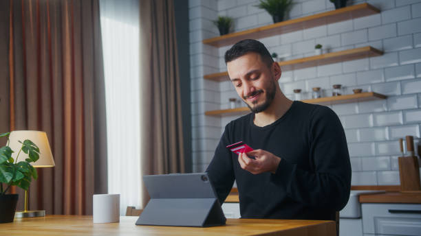istock Adult man enter credit card number on tablet and due insufficient funds experiencing problems during payment online with credit card while sitting in the kitchen 2012120762