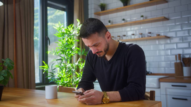 istock man sit in kitchen surfing internet on mobile phone, reading media news, scrolling social networks, using mobile applications on smartphone at home 2012127452