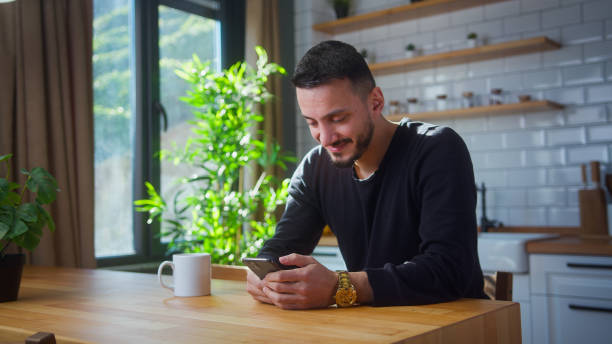 istock Smiling man sit in kitchen surfing internet on mobile phone, reading media news, scrolling social networks, using mobile applications on smartphone at home 2012133148