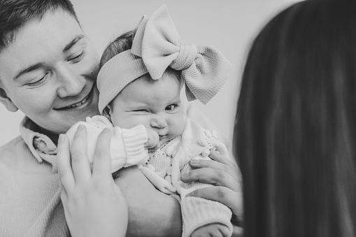 Close up black and white image of a dad and mom tenderly kissing their newborn baby.