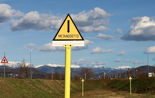 Metanodotto, natural gas pipeline in english language. Public yellow warning triangle signs in eastern border of Italy under a blue cloudy sky
