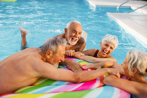 Group of cheerful mature friends having fun during summer day on a pool raft.