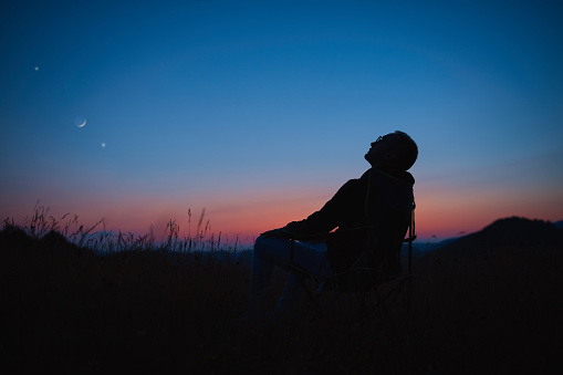 Man looking at the starry skies, crescent Moon and planets in blue hour twilight time.