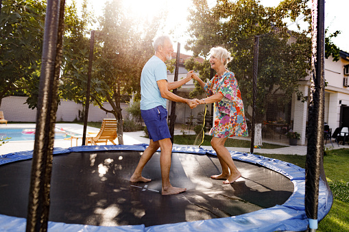 Cheerful mature couple having fun while playing on trampoline in the backyard.