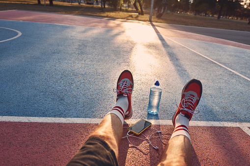 Sportsman training sneakers, smartphone with earbuds and bottle of water on a sports outdoor court.
