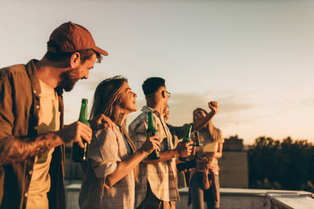 Cheerful friends having fun while drinking beer on a roof. - foto de acervo