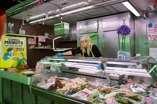 Horizontal view of a spotless offal stall with its owner in the old Abaceria Central Market of the Gracia neighborhood in Barcelona