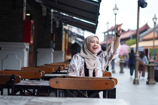 Indonesian Hijabi Woman Waving at a Distance or Calling the Cafe Attendant or Calling her Friend