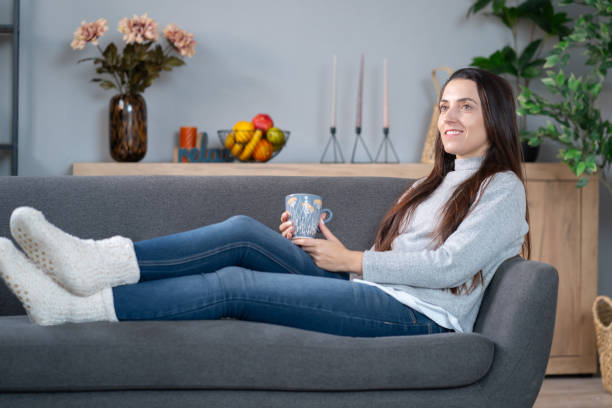 istock A young woman is laying on the sofa and drinking a cup of tea 2012244539