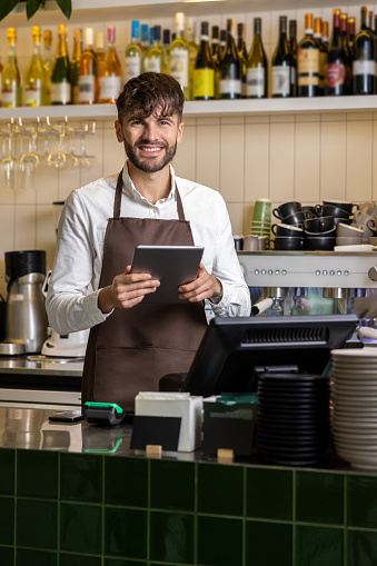 Handsome bearded man bartender standing with digital tablet at coffee shop counter