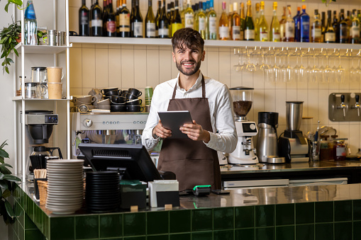 Happy man or waiter in apron with tablet pc computer at bar or coffee shop