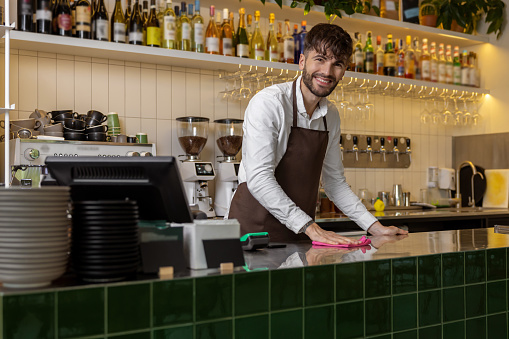 Bearded male barista wiping bar counter at work in cafe