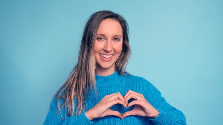 Happy young woman making a heart with her hands on a blue background