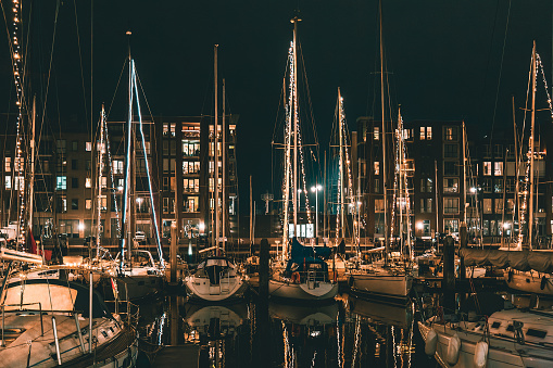 Scenic panorama of Scheveningen harbour is one of districts of The Hague, Netherlands. Romantic modern seaside resort. Brown brick buildings, light windows, moored white yachts and sailboats in evening.