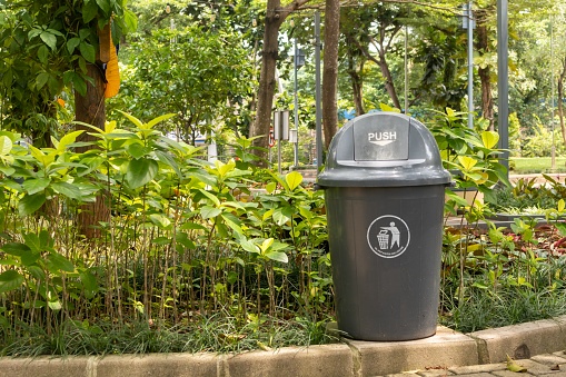 A gray plastic trash can with lid in the park