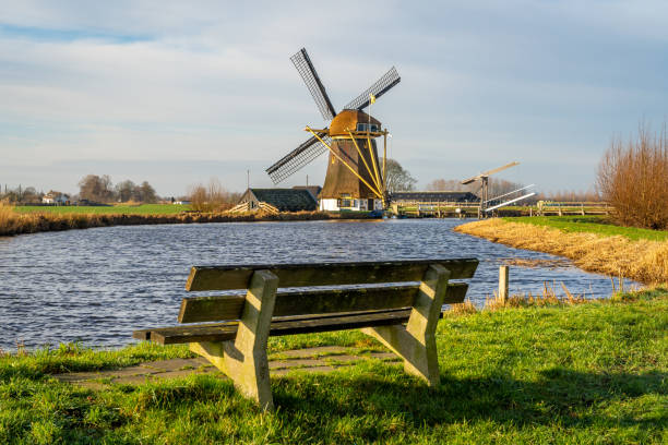 Scenery with historical dutch windmill by the river and empty bench