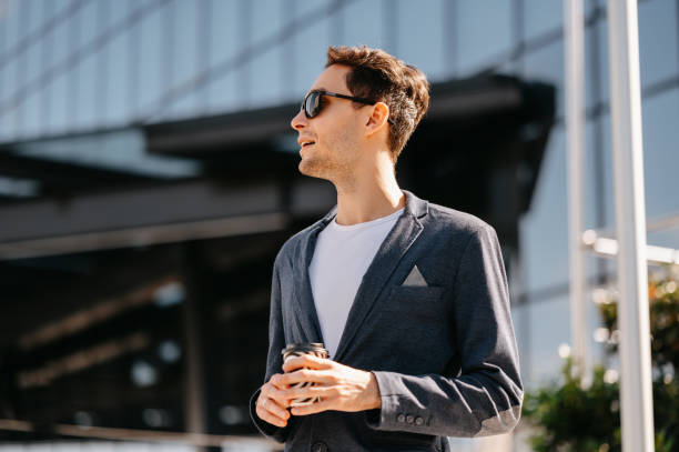 istock Handsome young man wearing jacket is looking aside while holding a coffee cup. 2012368342