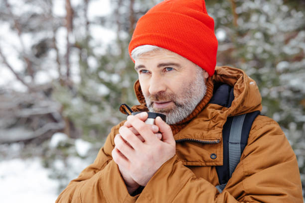 istock Bearded gray-haired man in red hat with thermos in hands in a winter forest 2012386786