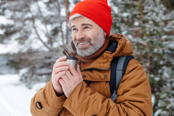 istock Bearded gray-haired man in red hat with thermos in hands in a winter forest 2012386798