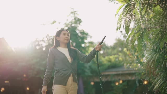 An Asian woman enjoys watering plants in the garden