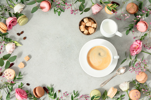 White cup of coffee and Frame made of Spring flowers and different types of macaroons flat lay mock up copy space