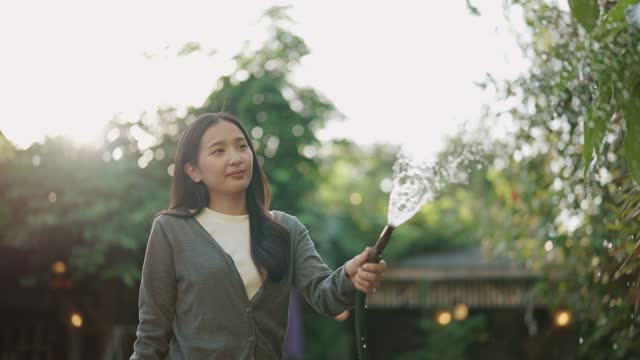 An Asian woman enjoys watering plants in the garden