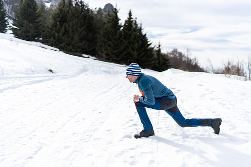 Healthy lifestyle. Man in sportswear stretching legs before running outdoors on snowy winter day