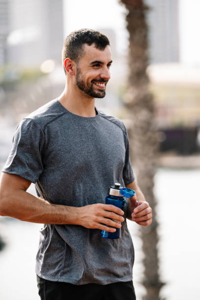 istock Happy active man drinks and recovery with refreshment after exercise outside. Young sports guy drinking water from bottle walking after workout in a park. 2012393904
